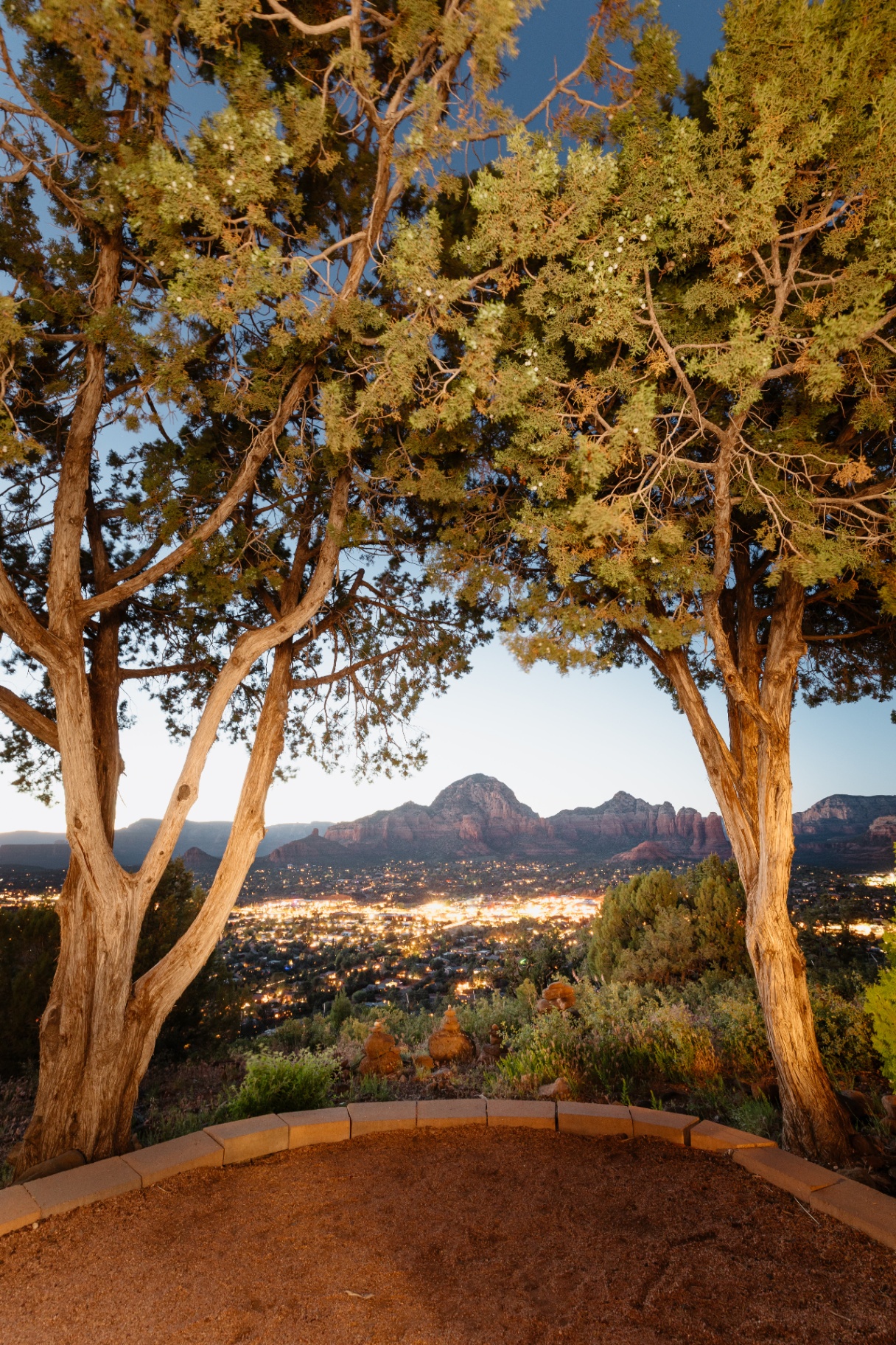 Sedona red-rock and city-light overlook framed by junipers at dusk