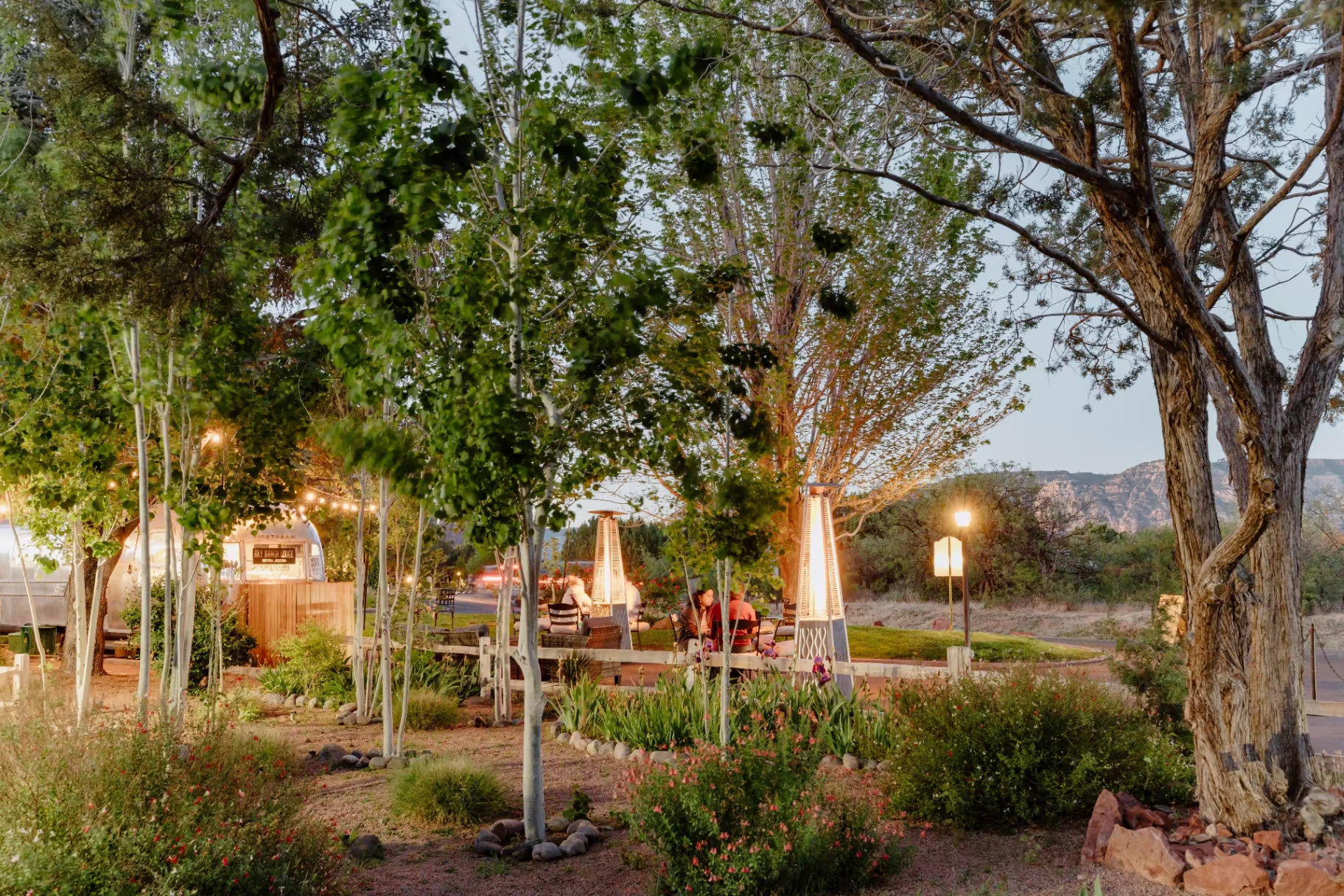 Evening patio and gardens at Sky Ranch Lodge with outdoor heaters and string lights among trees